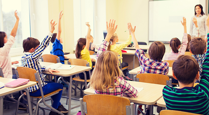 Crianças em uma sala de aula com as mãos erguidas.